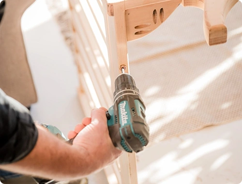 Hand assembling a wooden baby cot with a power drill